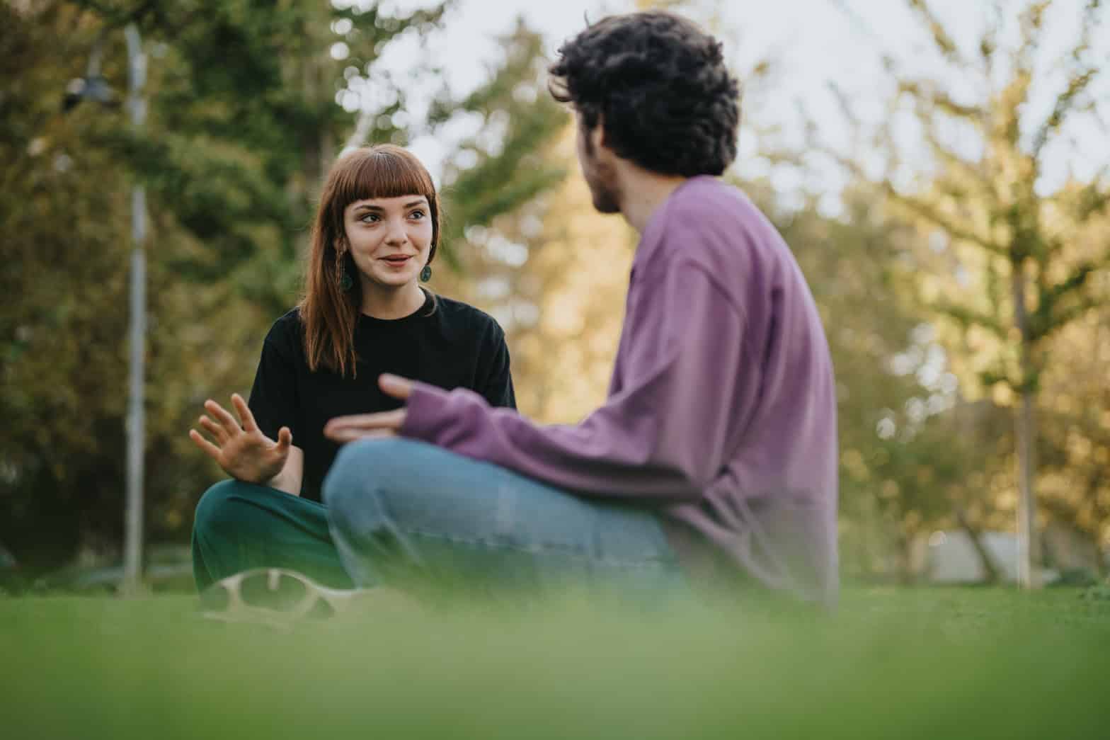 A young adult woman and a young adult man sitting on the grass having an indepth conversation