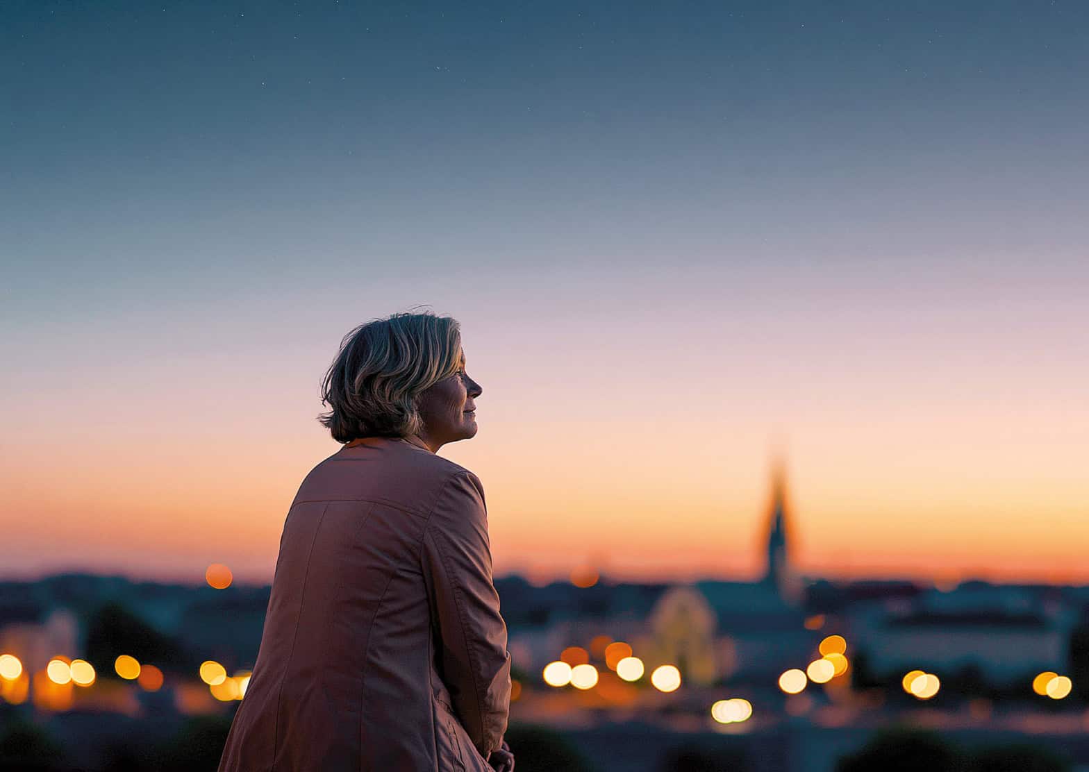 A lady looks optimistically towards the horizon with an orange sunset