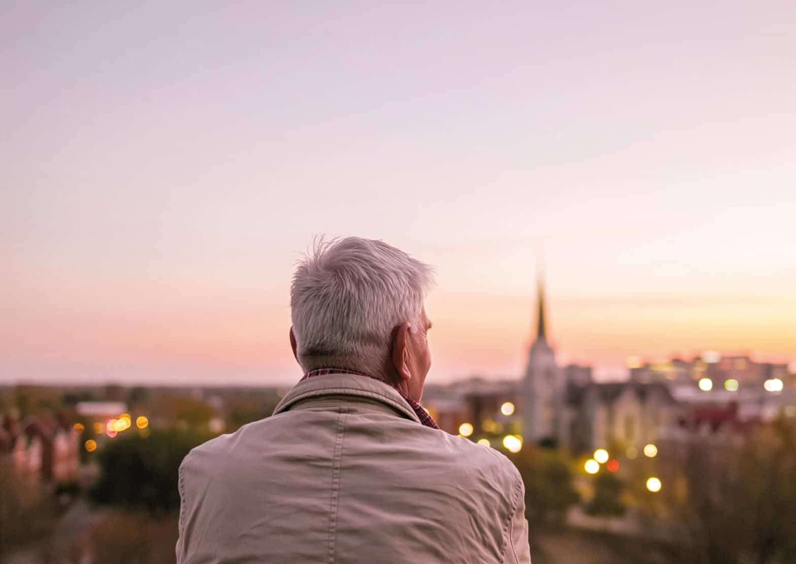 An older gentleman looks out optimistially towards the horizon with an orange sunset