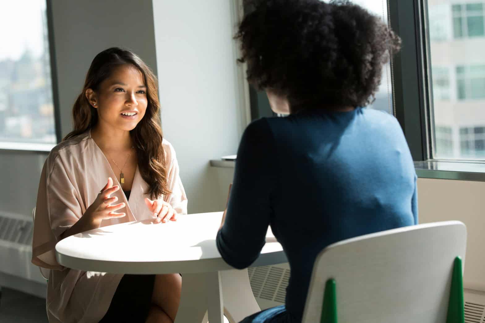 Two women sitting at a table in a light and bright room having a discussion