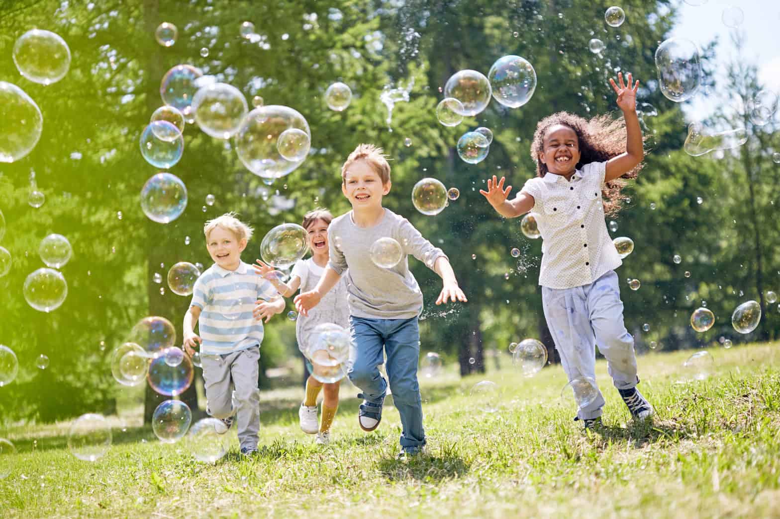 Diverse group of young children running outside in a green park chasing bubbles